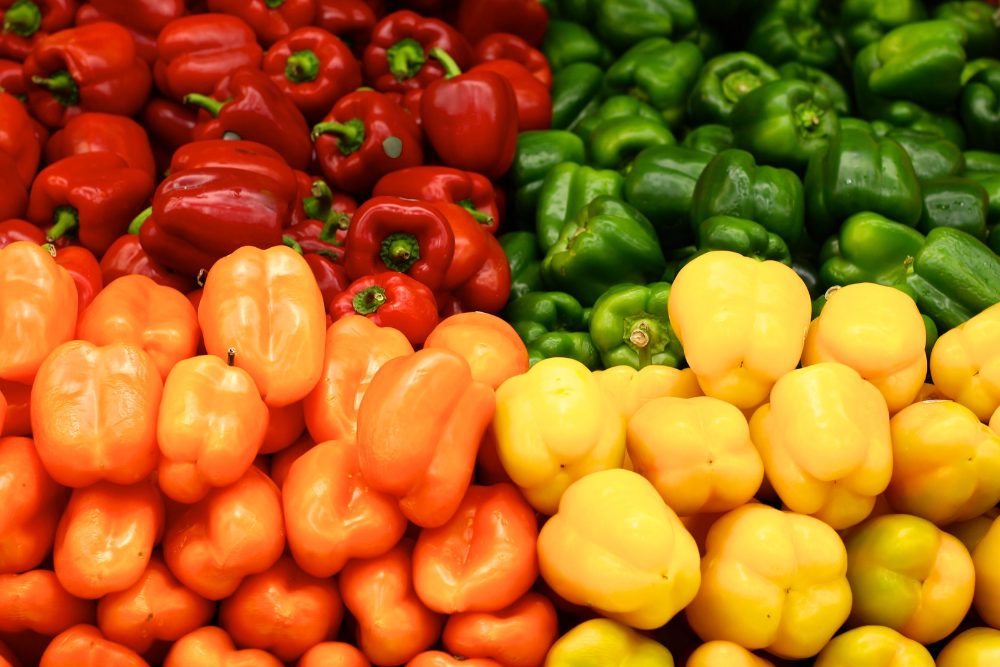 Red, orange, yellow and green bell peppers stacked in market crates