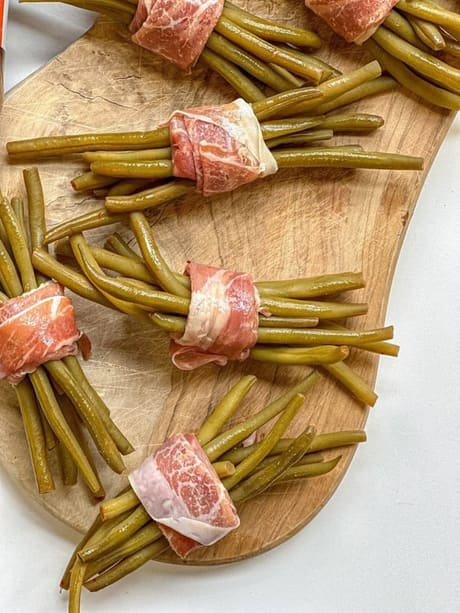 Prosciutto-wrapped pickled green beans plated on a wooden board