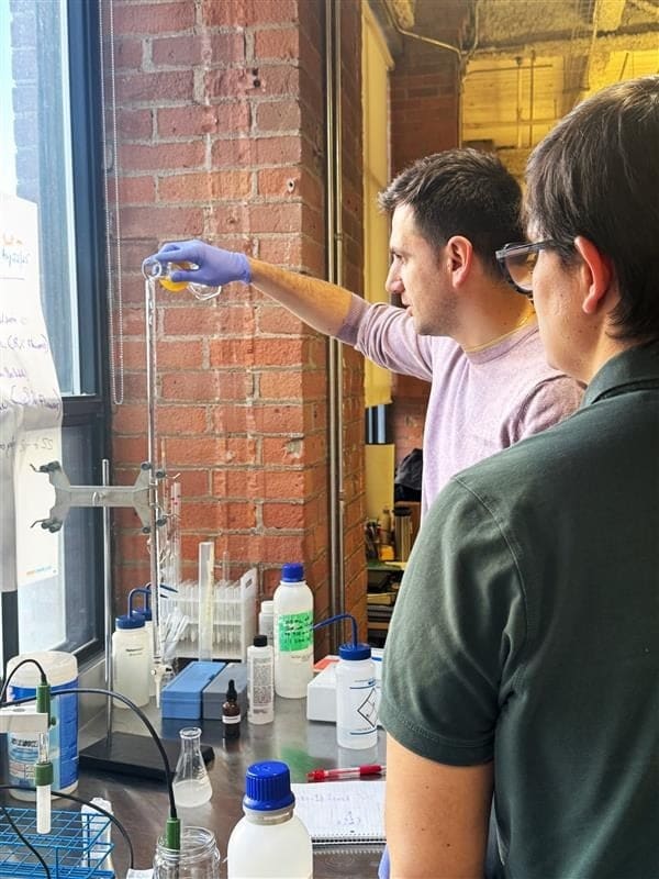 Two food scientists running a titration at a bench beside a brick wall