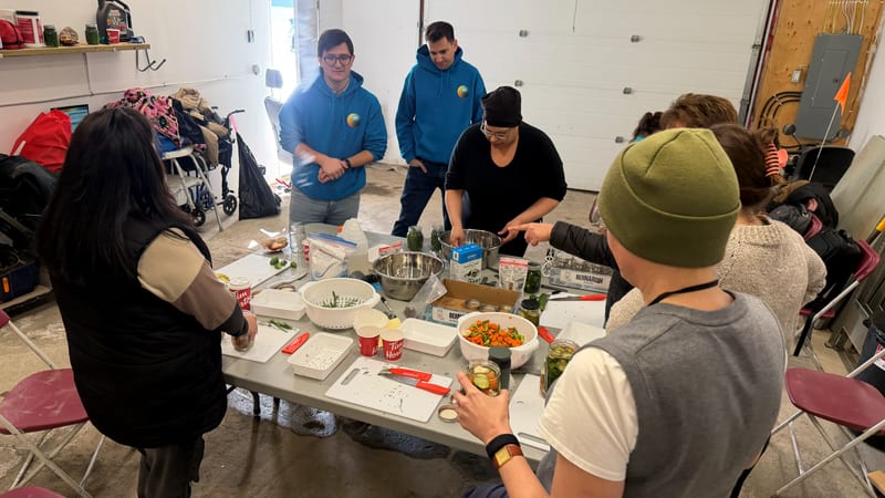 Participants around a table at a community food-preservation workshop, filling jars from bowls of green beans and diced carrots